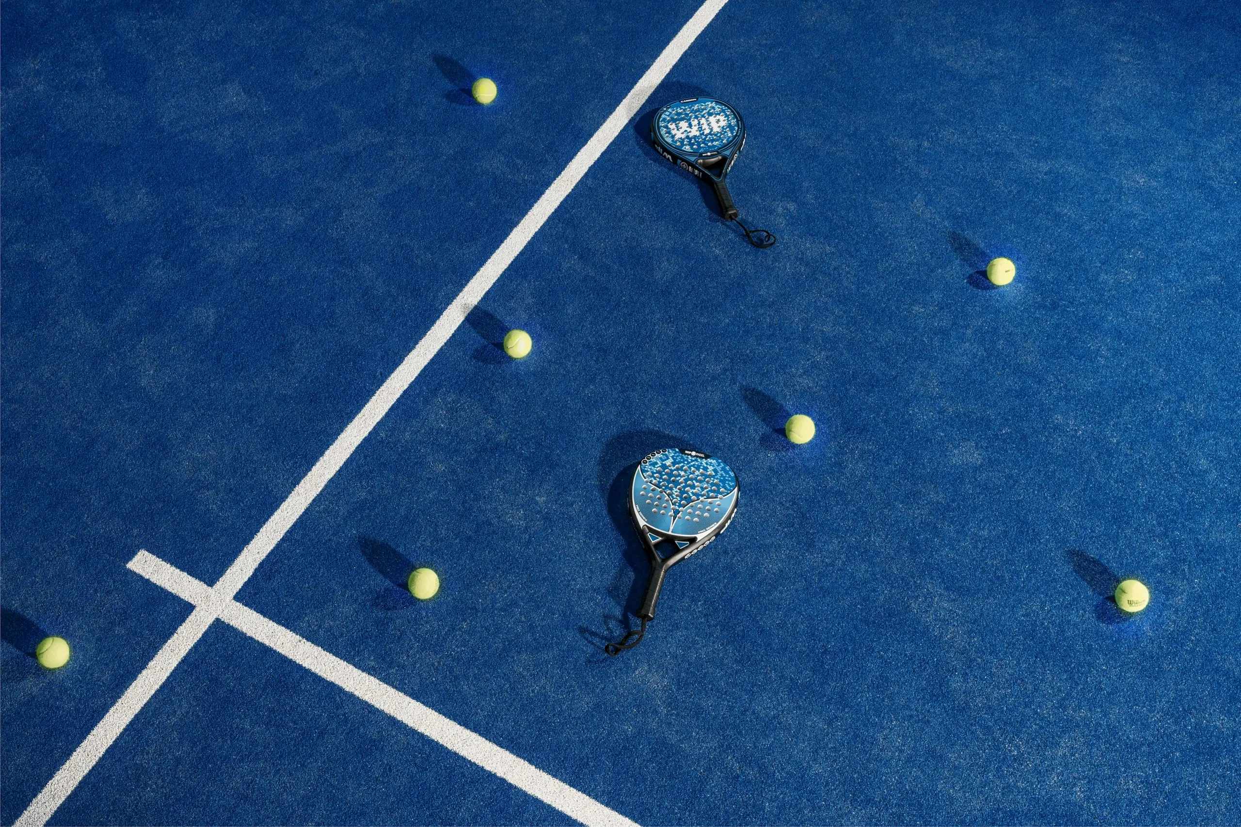 Twee padelrackets en ballen op de baan, van bovenaf gezien