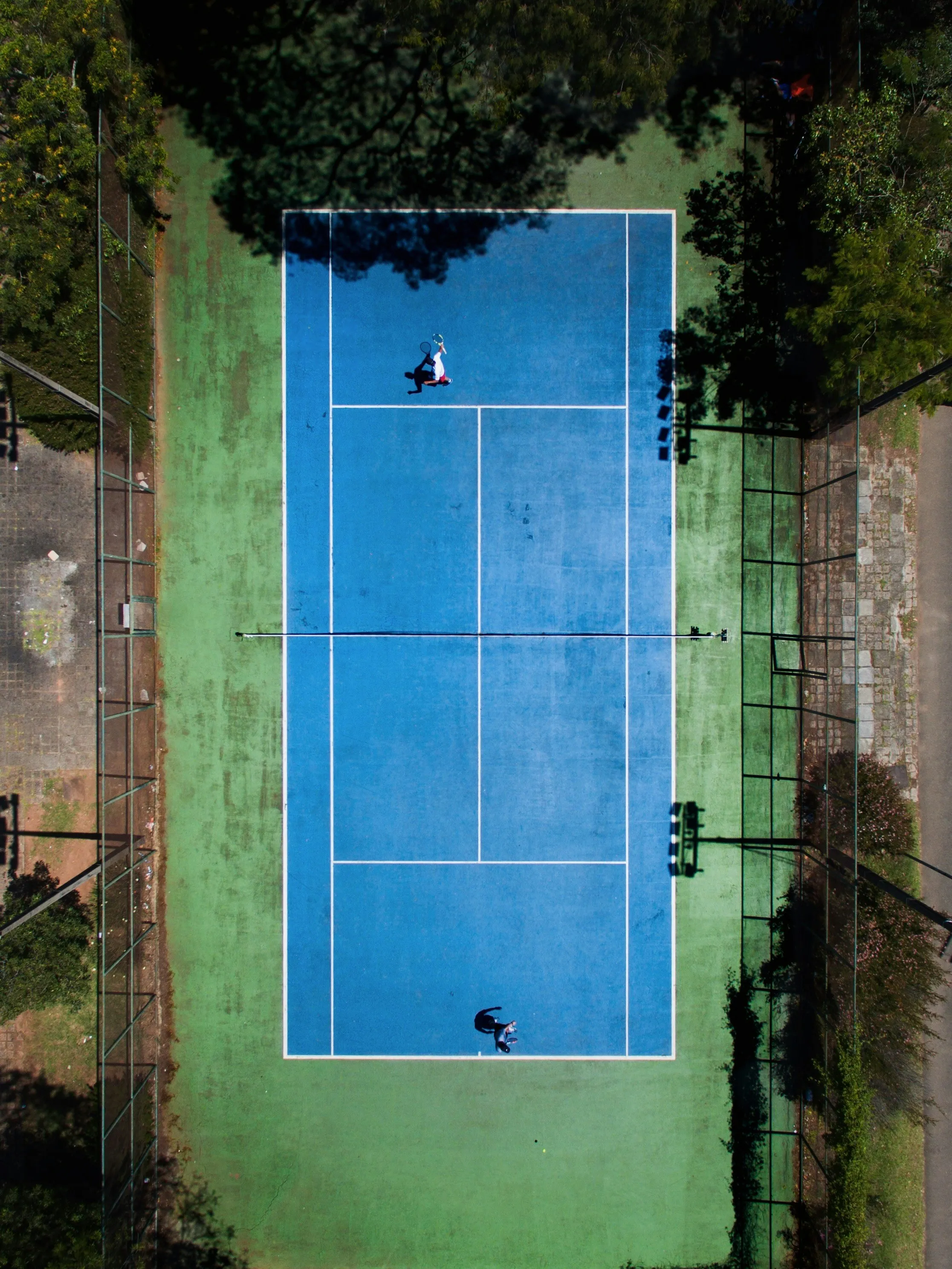 Tennisbaan van bovenaf met een speler aan de baseline